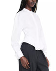 A woman wearing a white long-sleeve blouse with a high mock neck and black trousers, shown from the side against a plain white background.