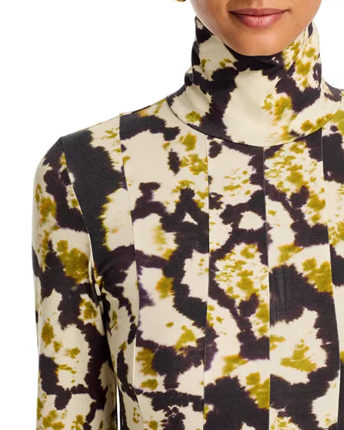 A close-up of a model wearing a long-sleeve mock neck top with a high-contrast abstract tie-dye pattern in black, olive green, and cream.