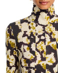 A close-up of a model wearing a long-sleeve mock neck top with a high-contrast abstract tie-dye pattern in black, olive green, and cream.