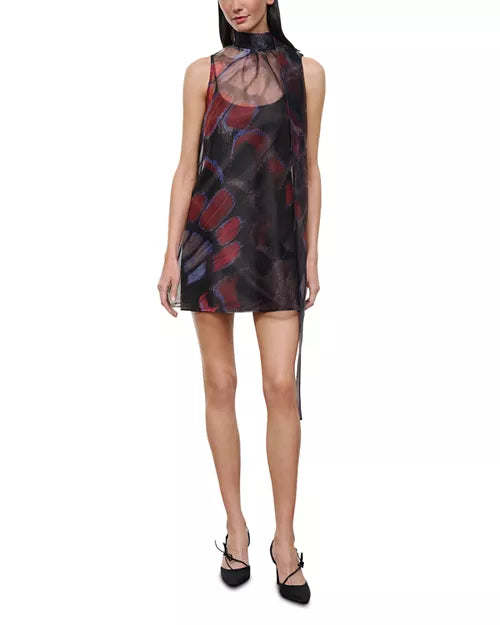 A model wearing a sleeveless high-neck mini dress made of sheer black mesh with a red and blue abstract floral print, paired with black lace-up heels, against a plain white background.