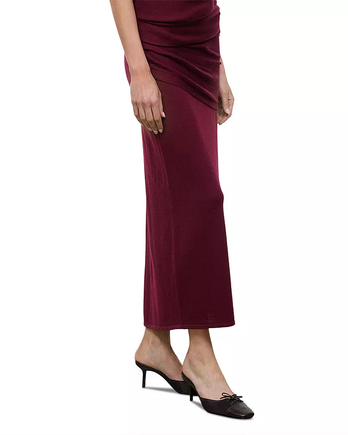 A model wearing a draped, floor-length wine red maxi skirt with black pointed-toe mule heels, shown from the waist down on a plain white background.