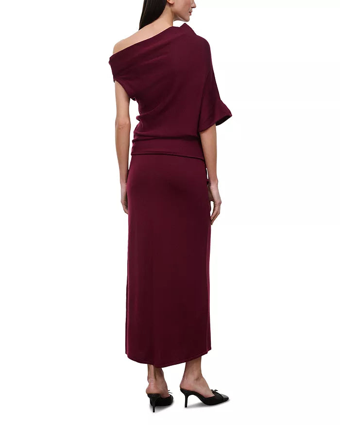 A woman modeling a deep burgundy off-the-shoulder maxi dress from the back, paired with black mule heels, against a plain white background.