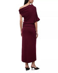 A woman modeling a deep burgundy off-the-shoulder maxi dress from the back, paired with black mule heels, against a plain white background.