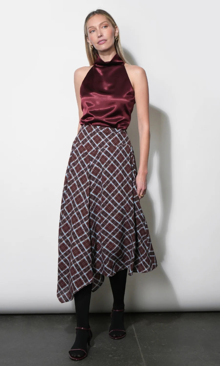 A woman modeling a sleeveless halter-neck top and matching plaid skirt set. The top is made of deep burgundy satin, while the skirt features a brown, white, and gray plaid pattern.
