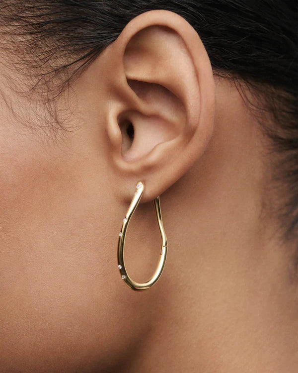Gold hoop earring worn on an ear with a blurred background