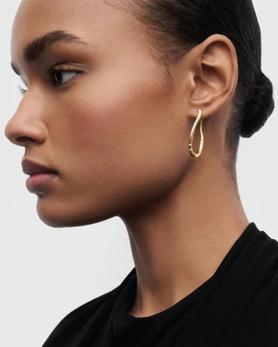 Close-up of a woman wearing a gold hoop earring against a neutral background