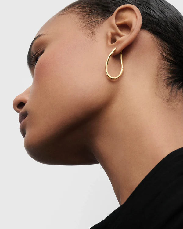 Close-up of a person wearing a gold hoop earring on a plain background