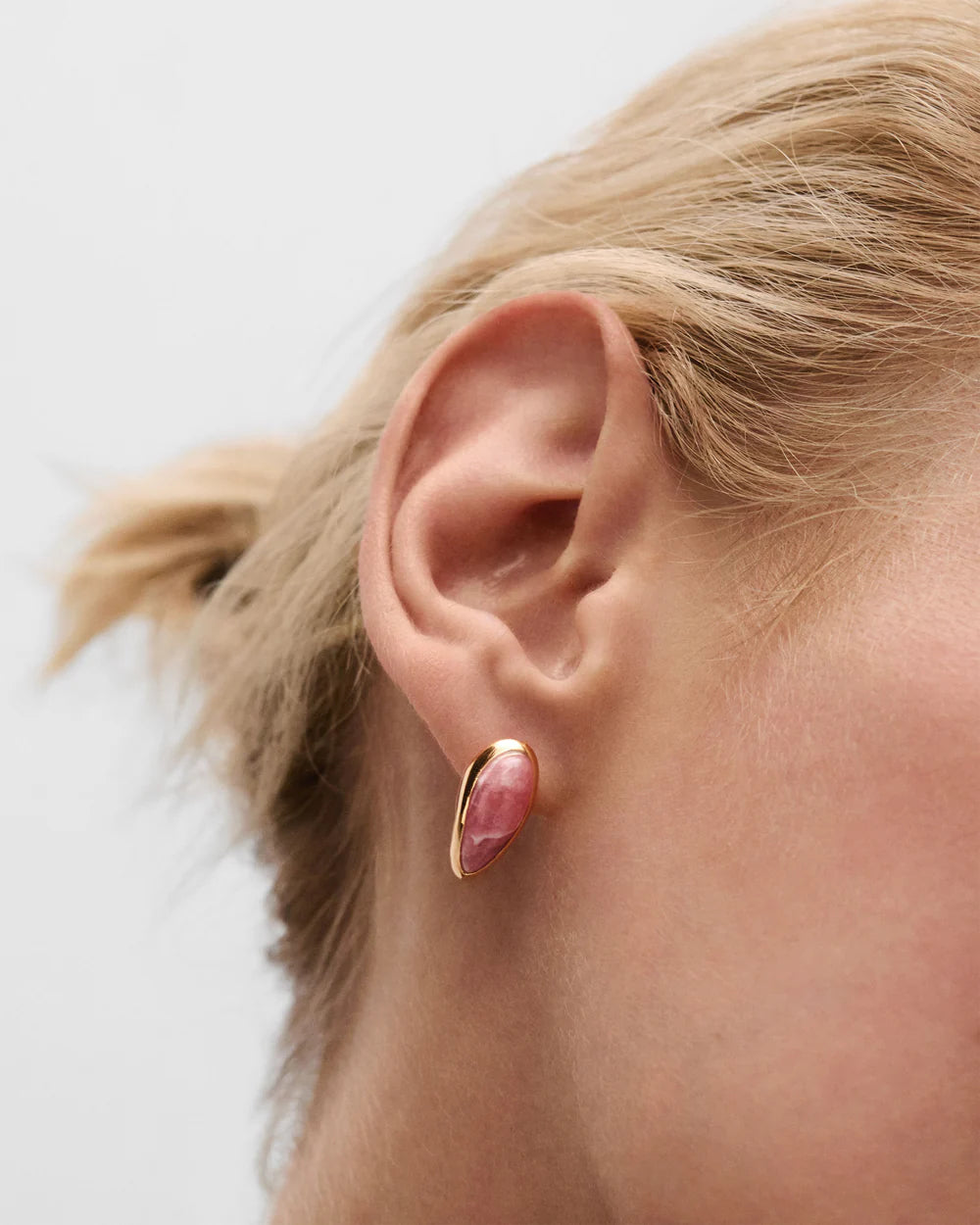 Close-up of a person wearing a pink gemstone earring with gold setting on a light background