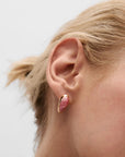 Close-up of a person wearing a pink gemstone earring with gold setting on a light background