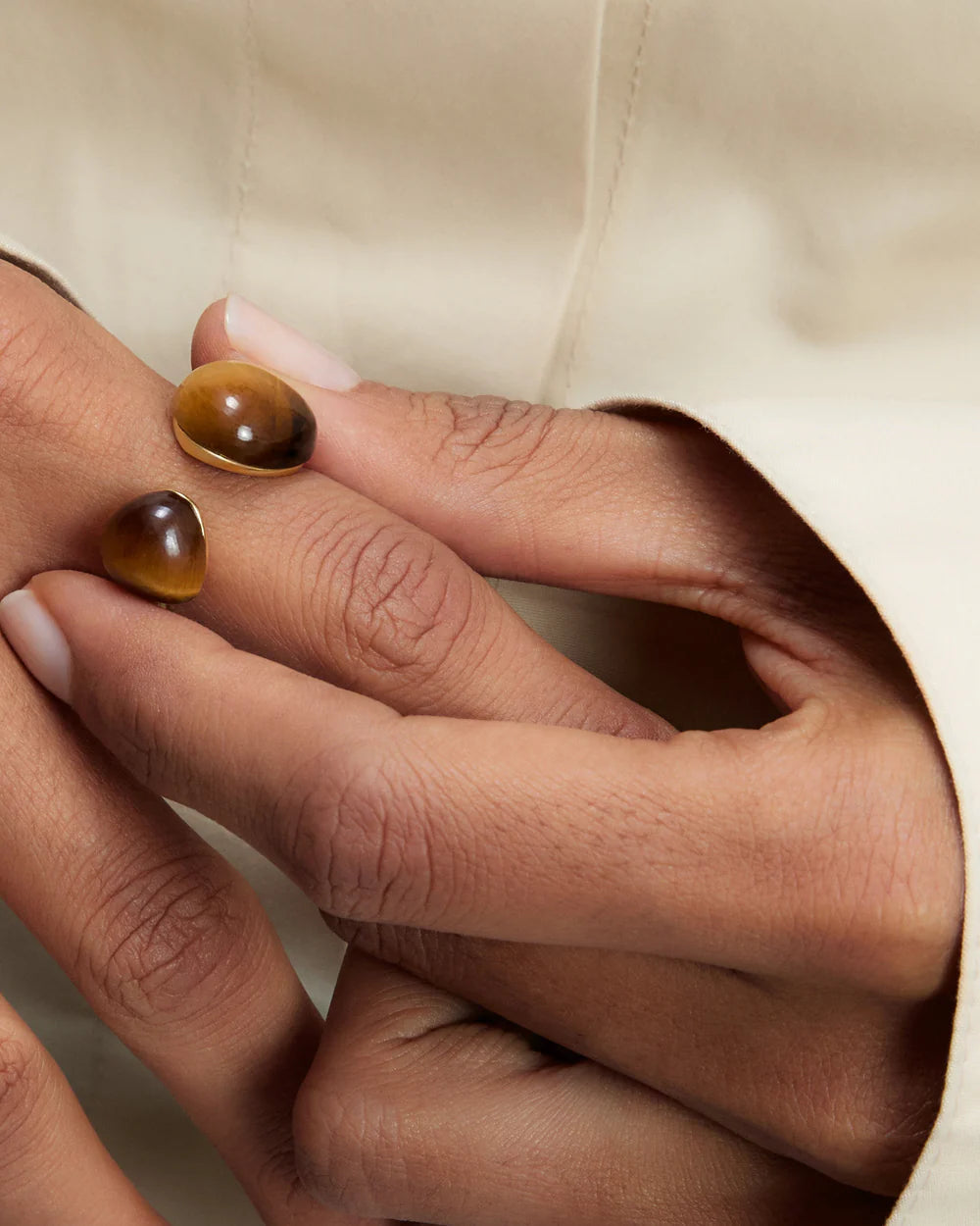 Close-up of hands wearing Tiger Eye Gravity Ring on a beige background