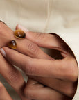 Close-up of hands wearing Tiger Eye Gravity Ring on a beige background