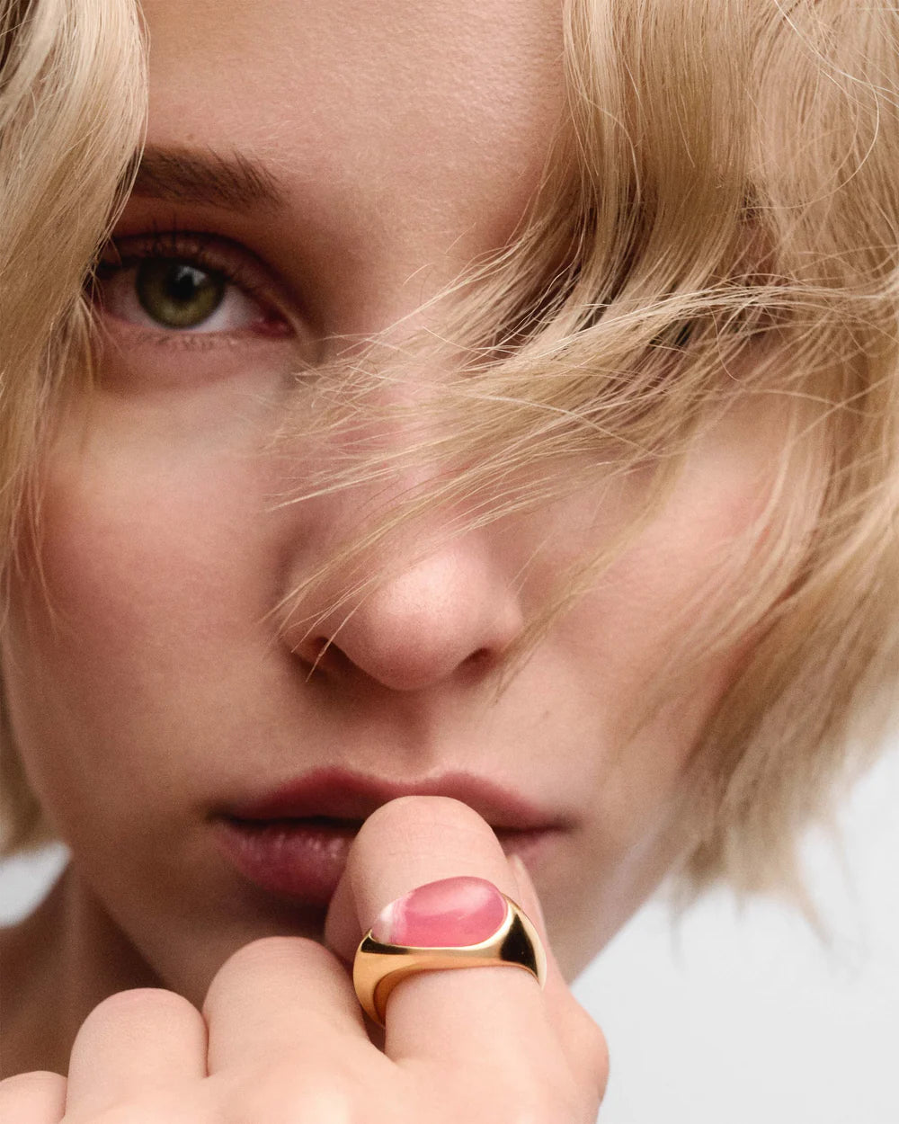 Close-up of a person wearing a gold ring with pink stone on a neutral background