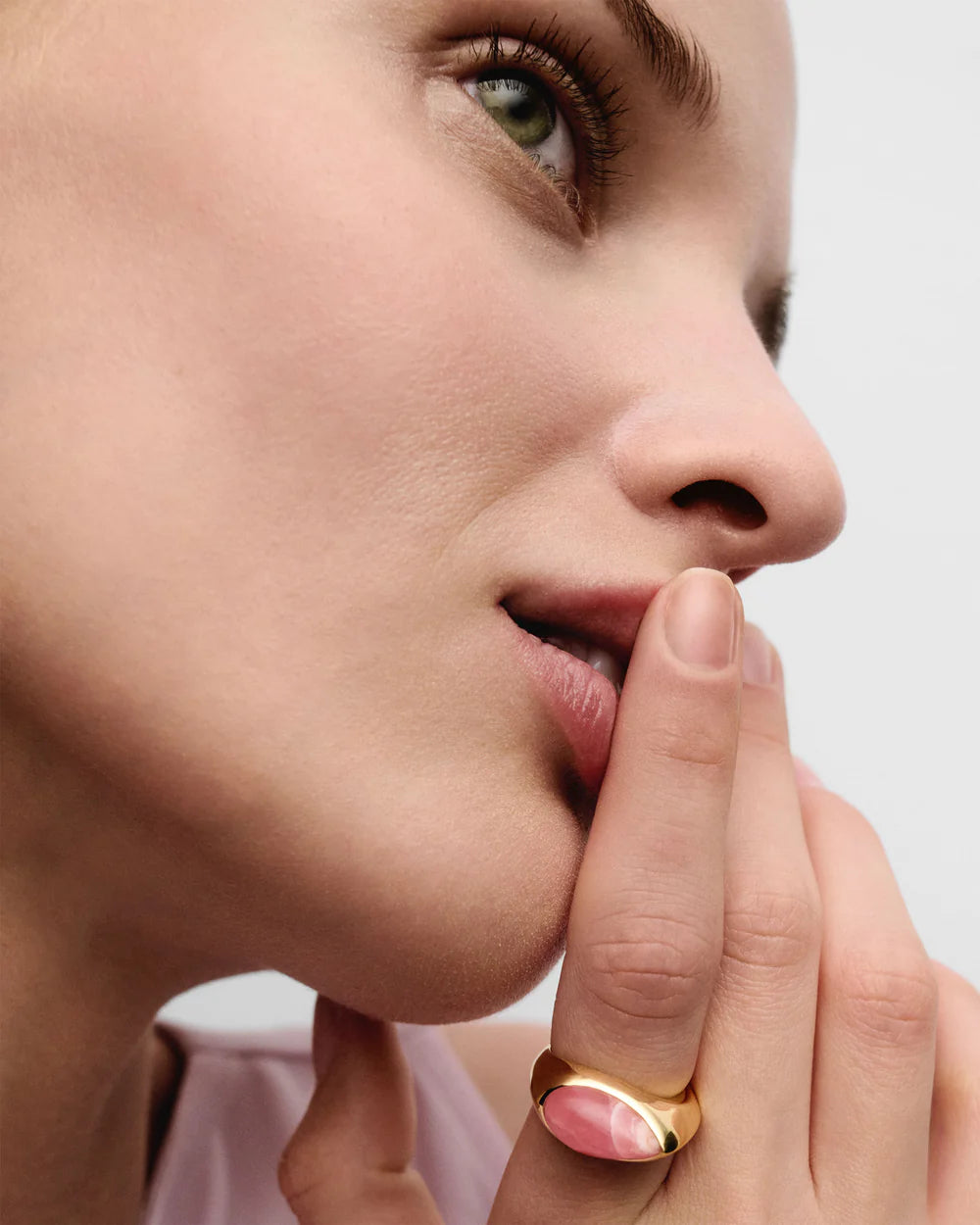 Close-up of a woman's face with Rhodochrosite Luna Stamp Ring on her finger, against a neutral background