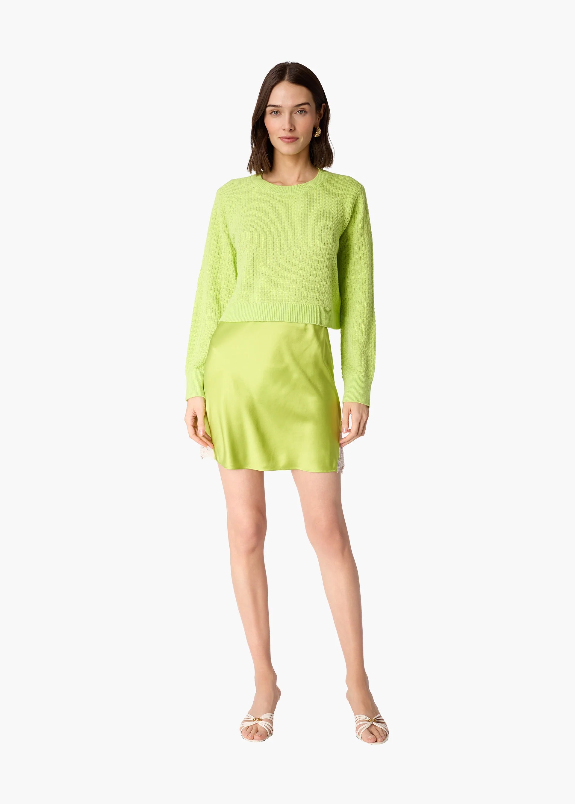 A woman modeling a bright lime green ribbed knit long-sleeve top and matching mini skirt set against a plain white background.