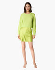 A woman modeling a bright lime green ribbed knit long-sleeve top and matching mini skirt set against a plain white background.