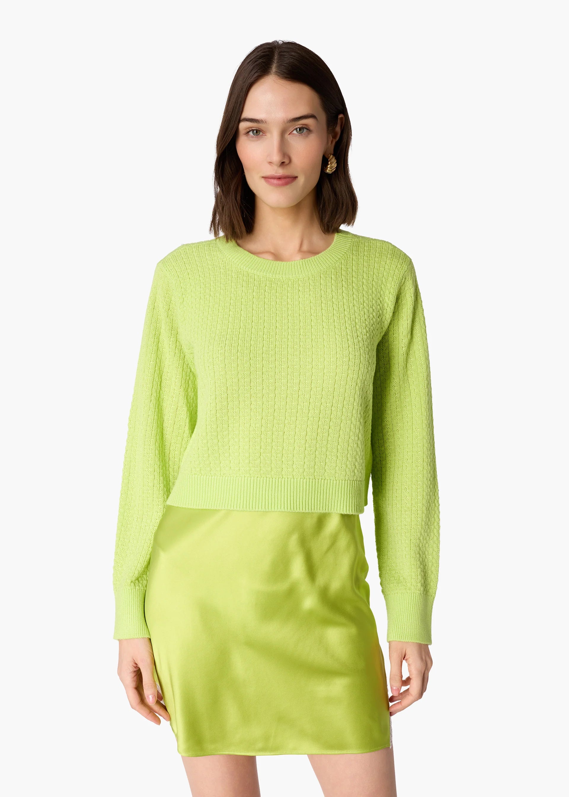 A woman modeling a bright lime green cropped long-sleeve sweater and a matching mini skirt, set against a plain white studio background.