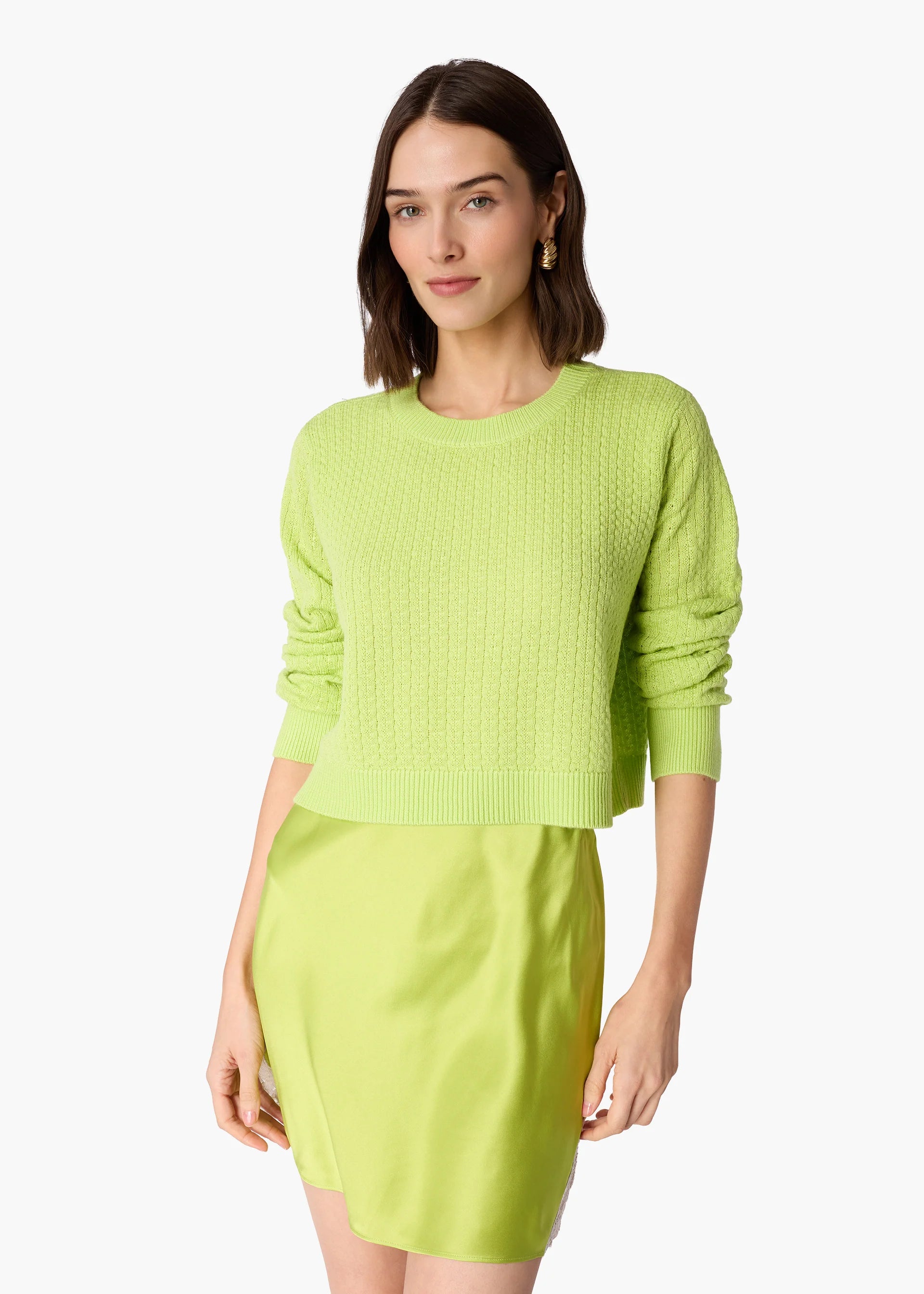 A woman modeling a bright lime green knit sweater with rolled sleeves and a matching lime green skirt against a plain white background.