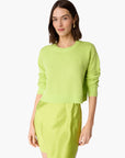 A woman modeling a bright lime green knit sweater with rolled sleeves and a matching lime green skirt against a plain white background.