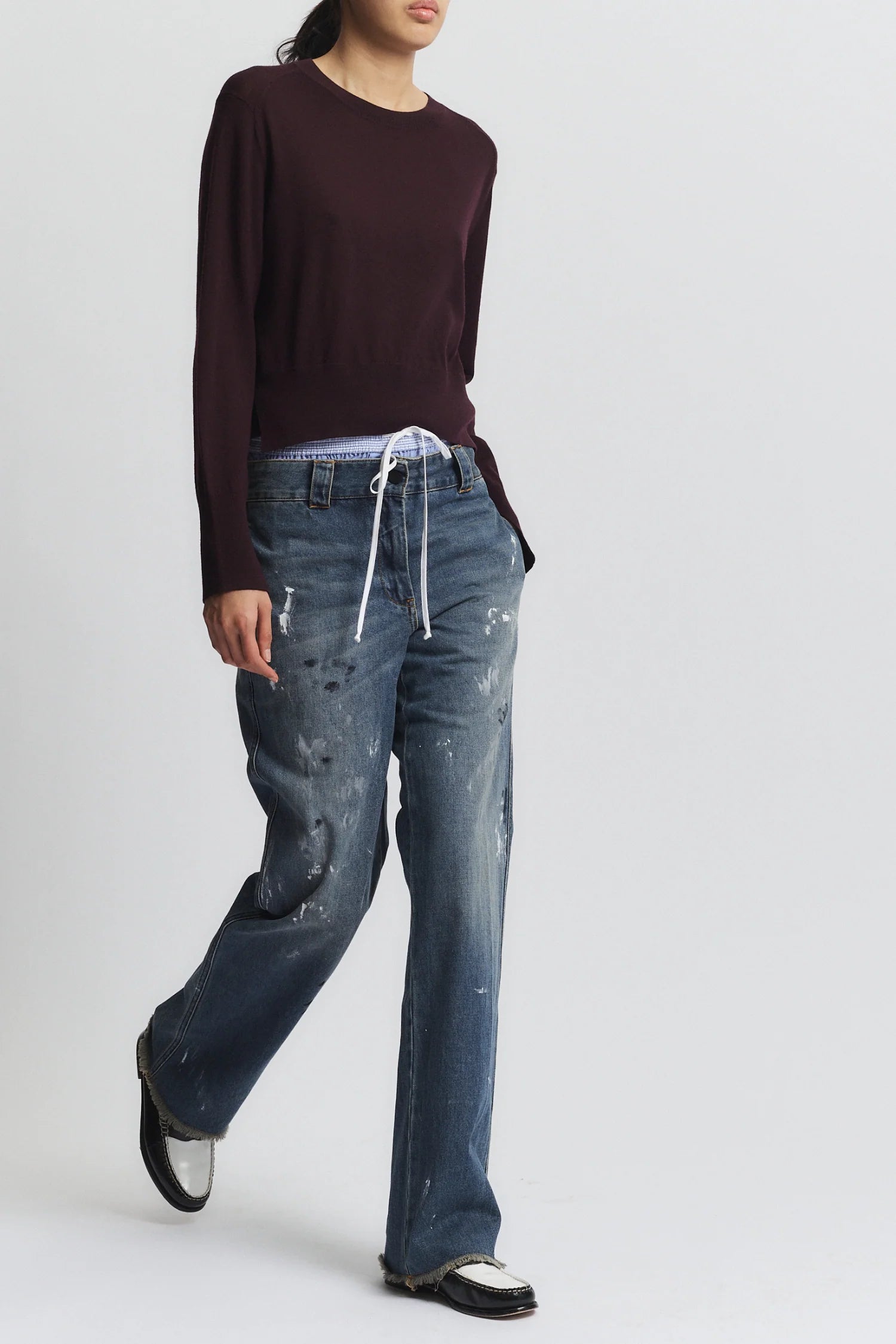 Person wearing a dark long-sleeve shirt and distressed blue jeans on a white background