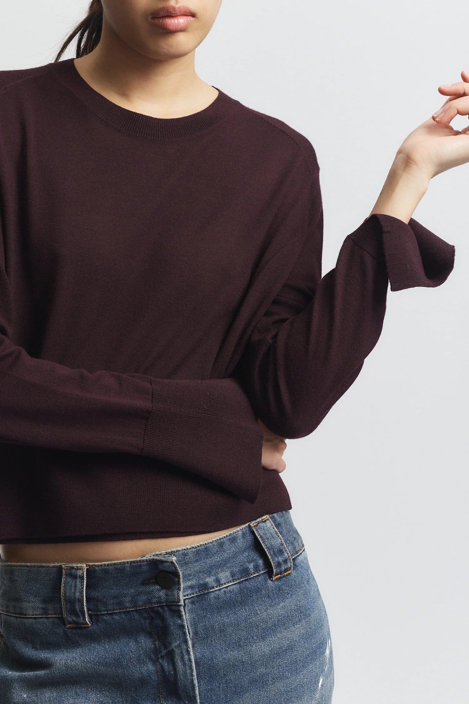 Person wearing a dark brown sweater and blue jeans on a light gray background