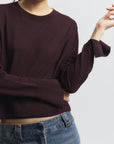 Person wearing a dark brown sweater and blue jeans on a light gray background