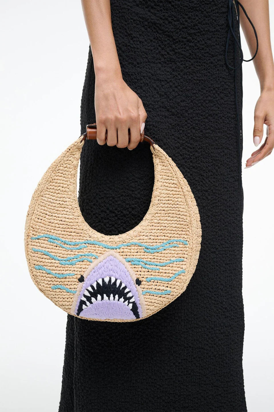 Woven handbag with shark design held by a person wearing a black dress.