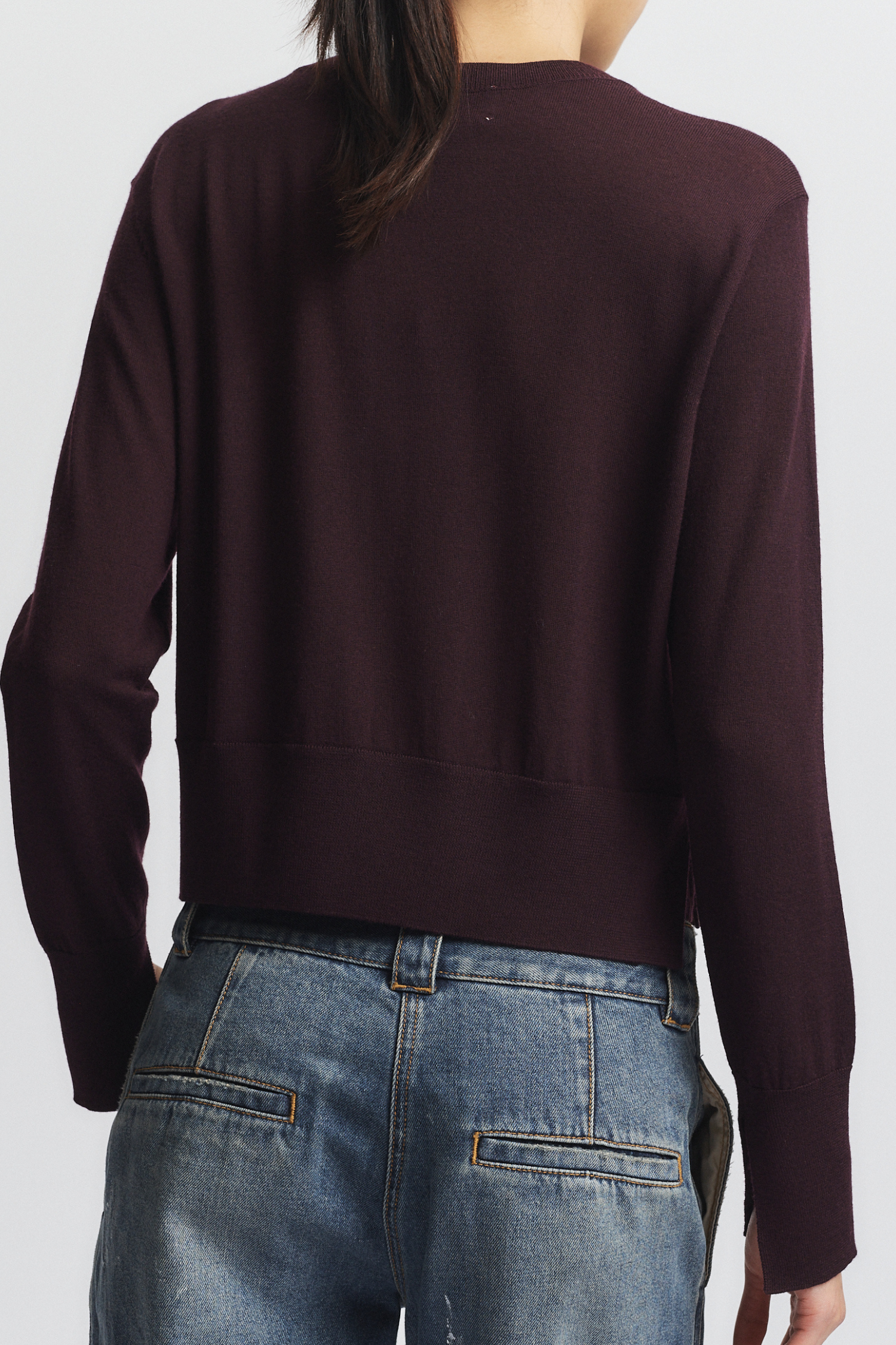 Person wearing a dark brown sweater and blue jeans on a white background