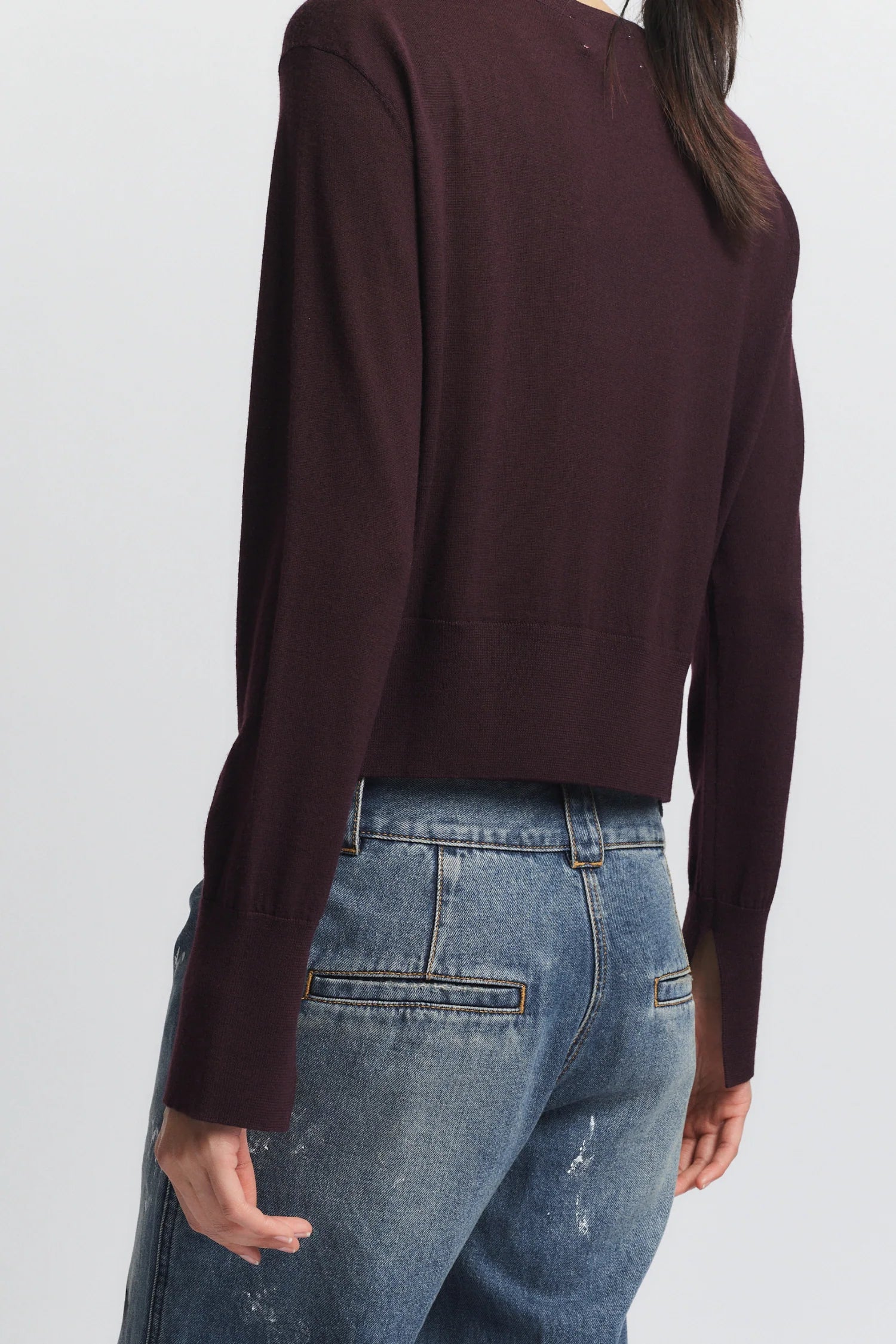 Person wearing a brown long-sleeve top and blue jeans on a white background