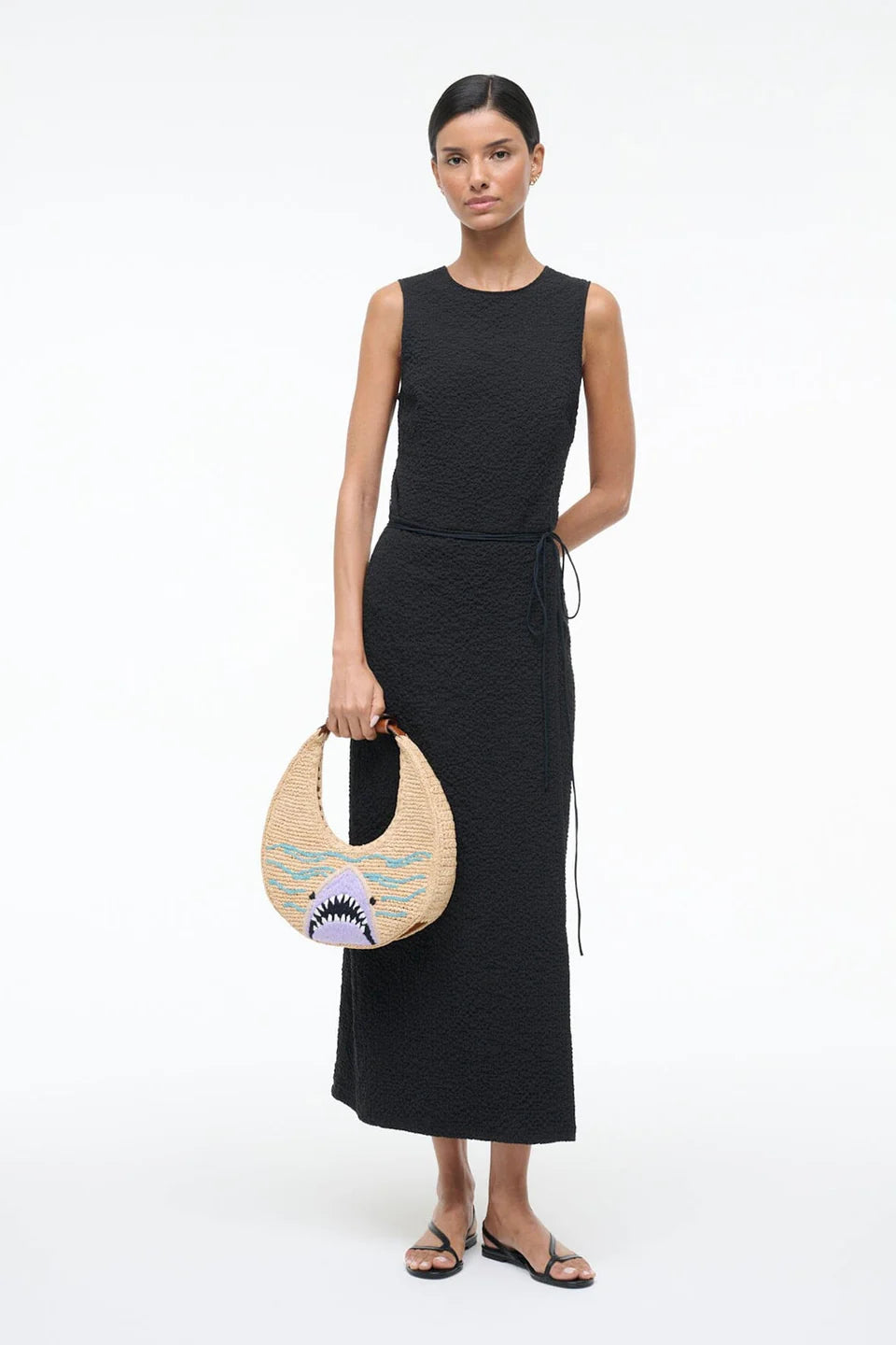 Woman holding a round straw bag with a shark design against a white background
