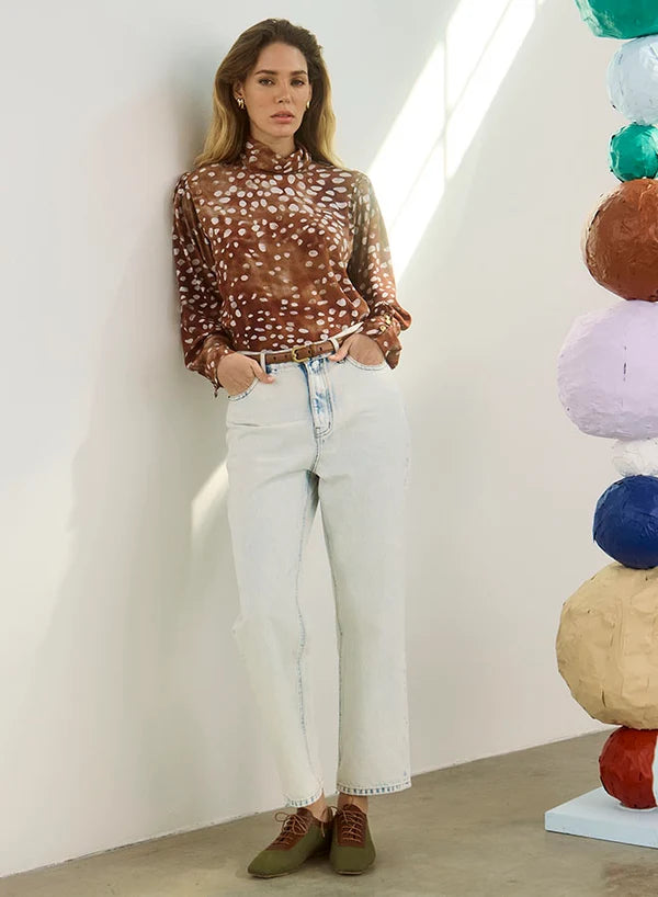 model wearing dapple doe printed top and jeans with art paper mache balls in the background
