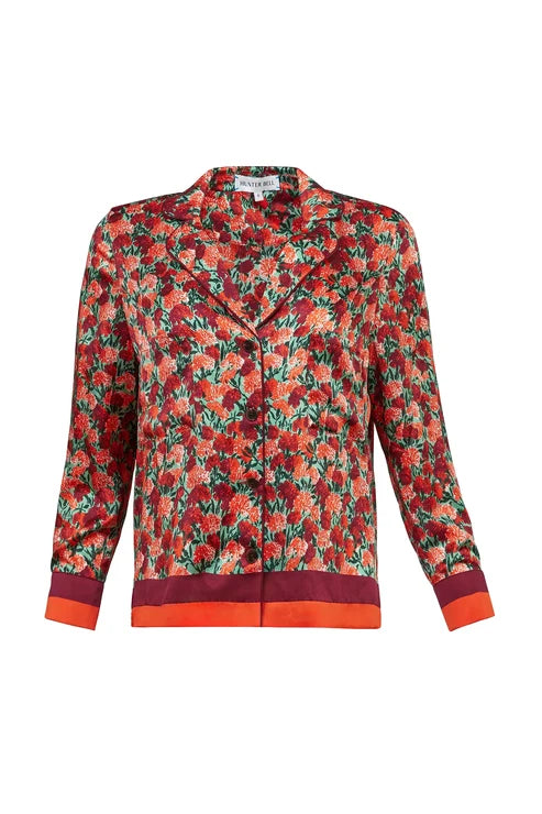 A long-sleeve button-front shirt jacket with a dense red, orange, and green floral print, featuring solid dark red cuffs and a matching dark red hem, shown on a plain white background.