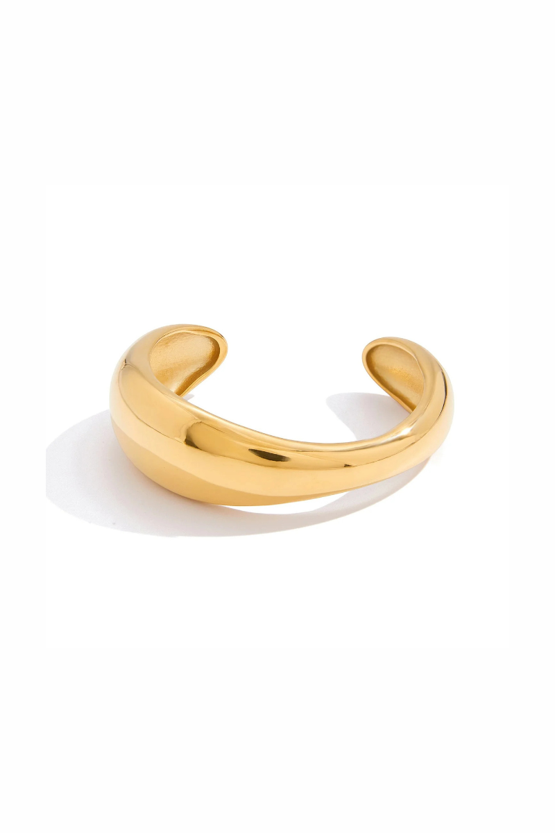 A polished gold-toned metal cuff ring with a smooth, curved design, displayed on a clean white background with a soft shadow.