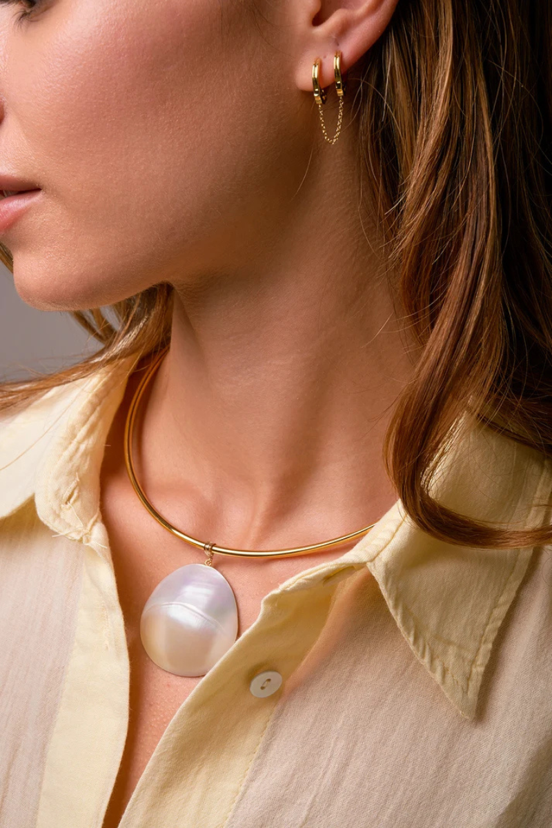 Close-up of a woman wearing gold hoop earrings and a gold necklace with a pearl pendant.