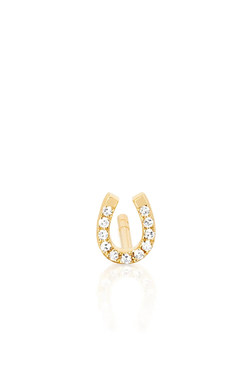 A gold horseshoe-shaped stud earring adorned with clear pavé gemstones, shown on a clean white background with a soft reflection below.