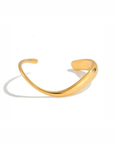 A polished gold-toned metal cuff bracelet with a smooth, curved design, displayed on a clean white background with a soft shadow.