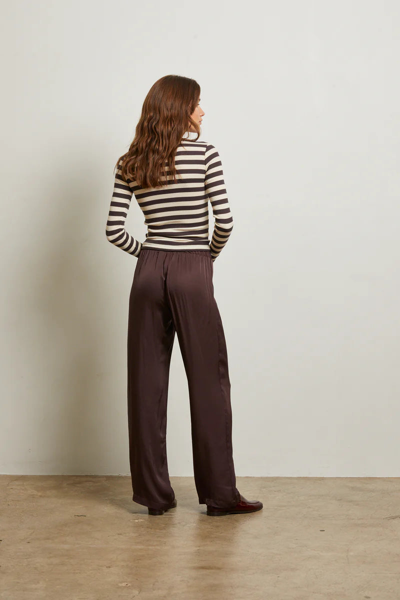 Woman wearing a striped sweater and brown pants against a plain background back view
