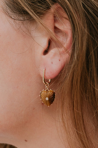 Close-up of a person wearing a gold earring with a brown stone.