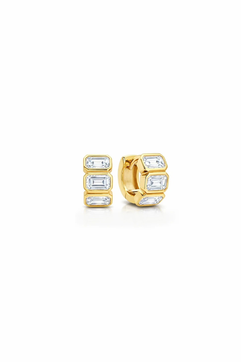 A pair of gold huggie hoop earrings with baguette-cut clear gemstones, shown on a plain white background.