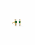 A pair of gold post earrings featuring a central green rectangular gemstone, flanked by small clear stones, shown on a plain white background.