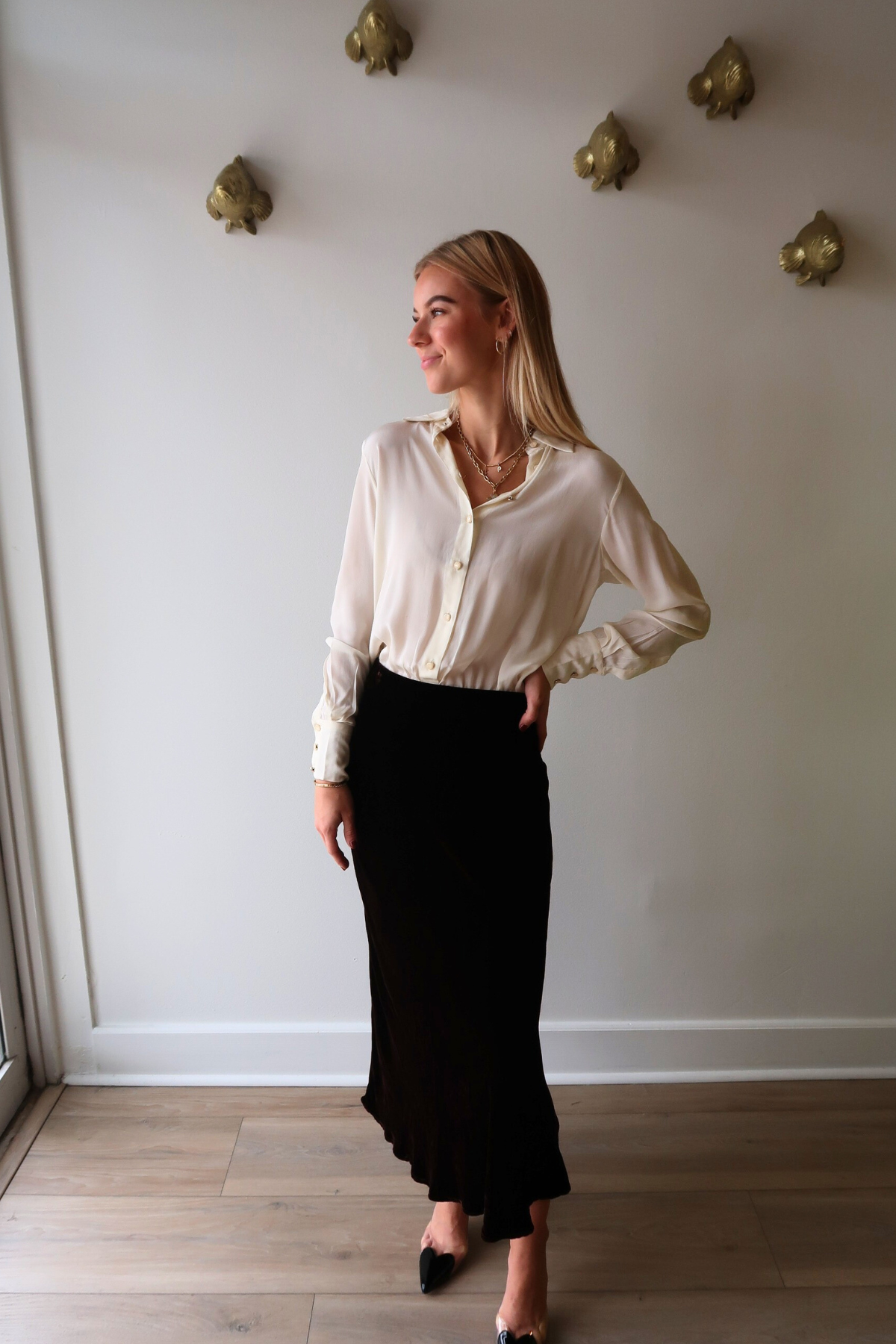 Woman wearing Alyssa Long Sleeve Bodysuit in Ivory and Felicity Velvet Midi Skirt standing against a plain wall.