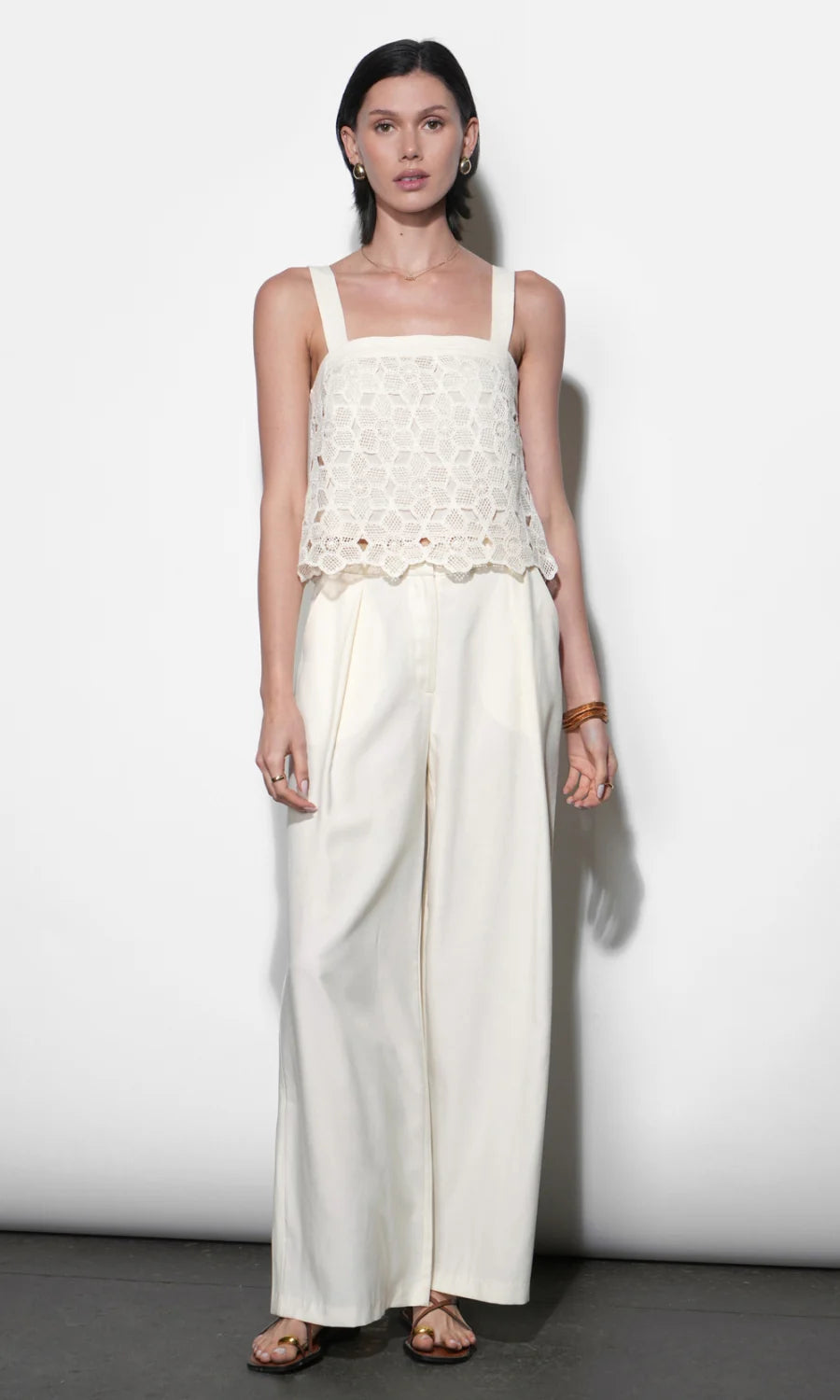 Woman wearing a white sleeveless top and wide-leg pants against a plain background