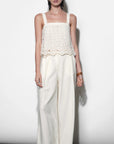 Woman wearing a white sleeveless top and wide-leg pants against a plain background