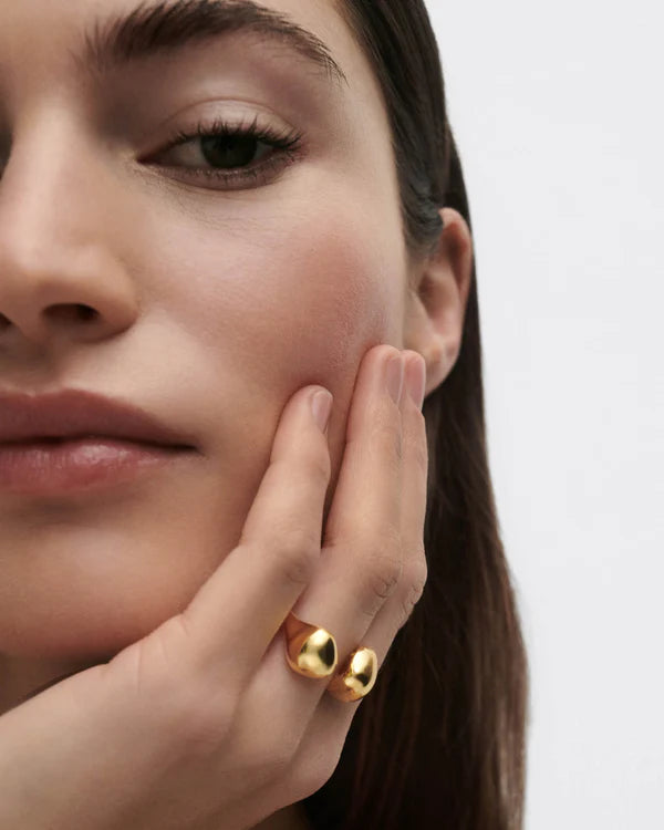 Close-up of a woman wearing a gold ring on her finger against a plain background