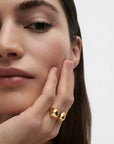 Close-up of a woman wearing a gold ring on her finger against a plain background