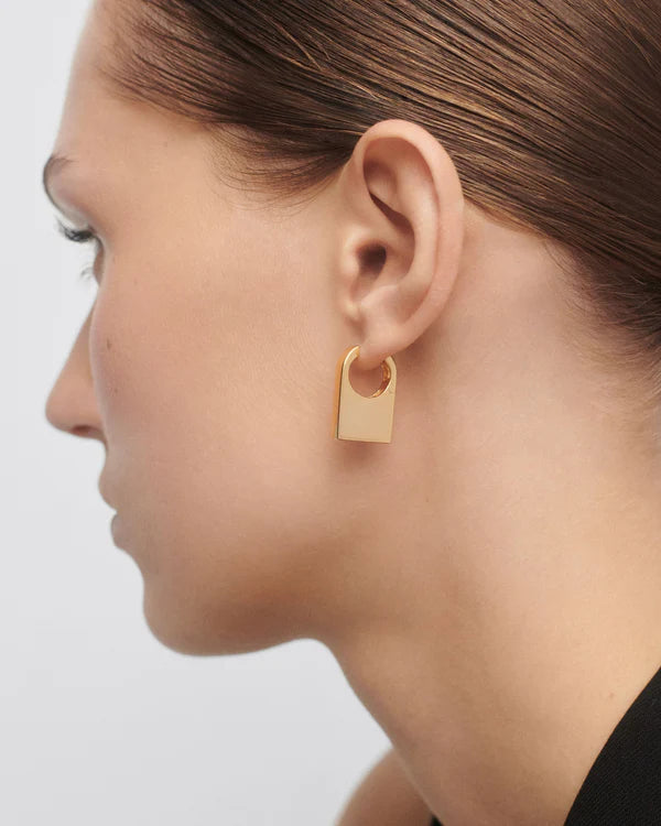Gold hoop earring worn by a person on a light gray background