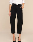 A model wearing black cropped trousers with side pockets, styled with a black belt, a white button-down shirt, and black heels against a solid beige background.