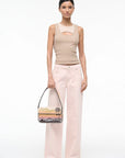 Woman wearing a beige sleeveless top and pink pants, holding a transparent handbag with a sunset design