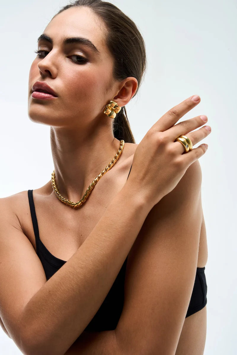 Woman wearing gold jewelry including earrings, necklace, and ring on a white background