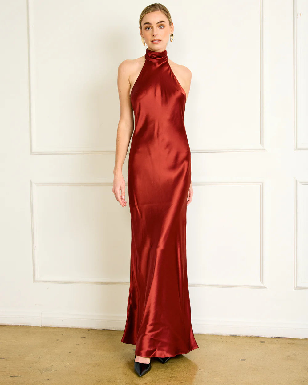 Woman wearing a red satin halter neck gown against a white wall.