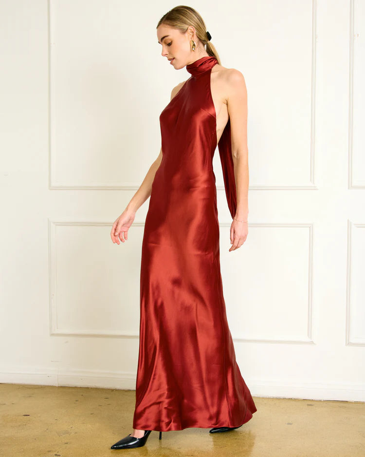 Woman wearing a red satin halter neck gown against a white wall, side/front